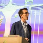 Bob Beard speaks at a podium in front of an image of the city from the cartoon "The Jetsons"