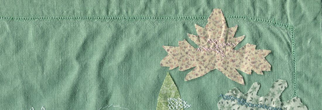 Green linen embroidered with the white outline of a squirrel, and five leaf shapes cut from multiple colors of fabric secured to the linen with cross stitches in various colors.