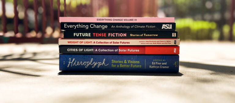 A stack of books on the ground, against a blurry outdoor backdrop.