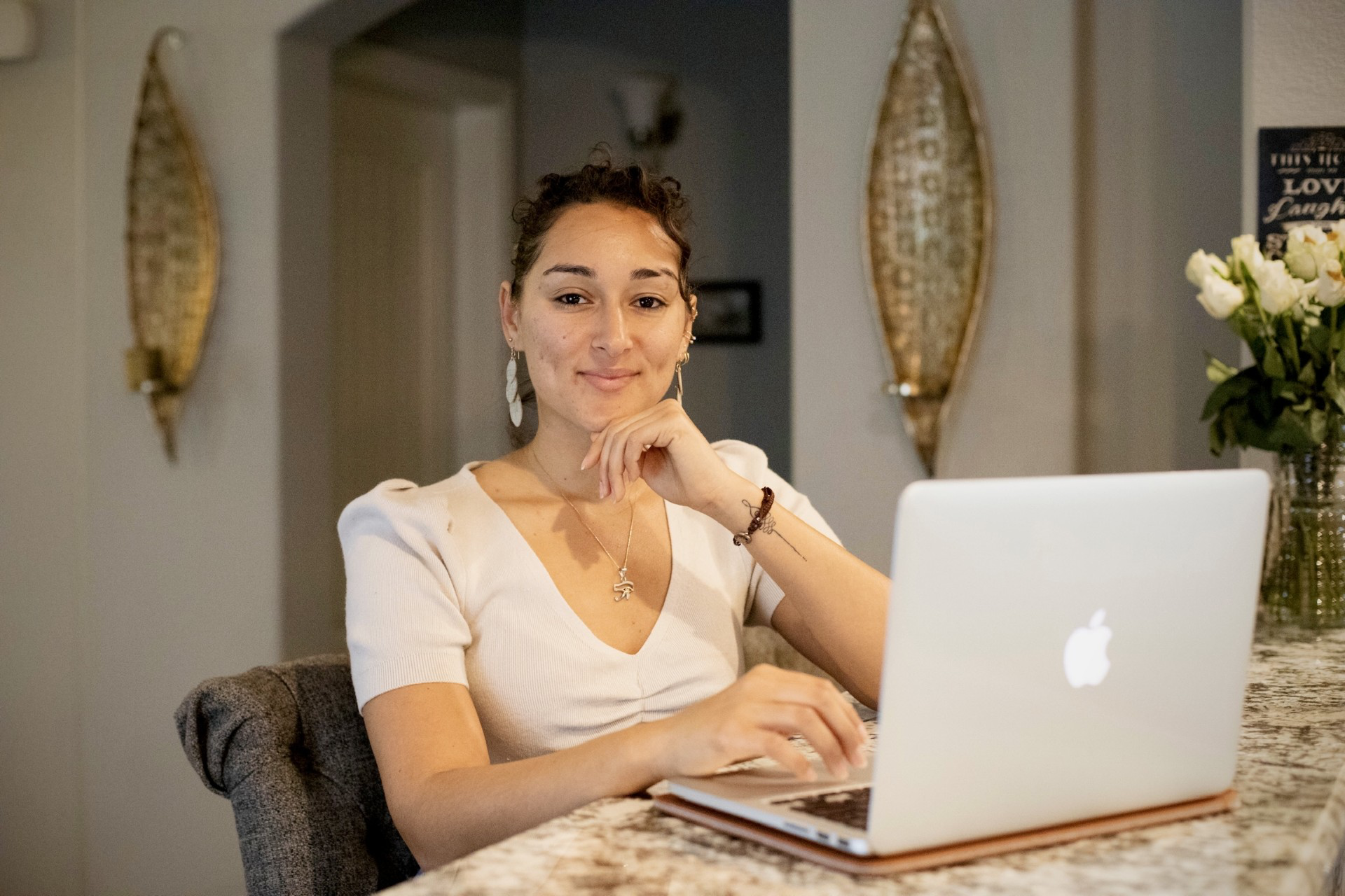 Eliza DelaPaz sits at a desk in front of a laptop looking at the camera with a pensive smile