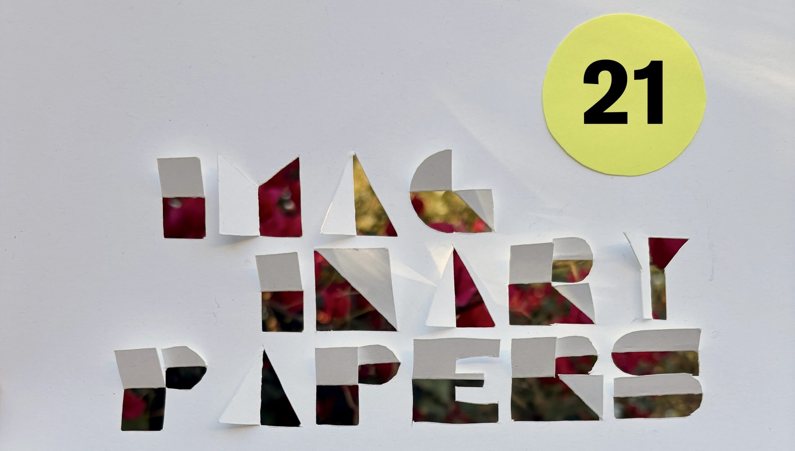 Imaginary Papers banner, with white paper cut out and folded to form letters with the brightly colored sheets below. In the top right corner, the number 21 is printed in black on a yellow circle of paper.